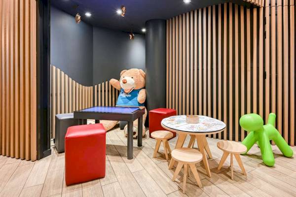 Kinderecke im Novotel Paris Centre Bercy mit Teddybär, Tisch, Stühlen und Spielzeug.