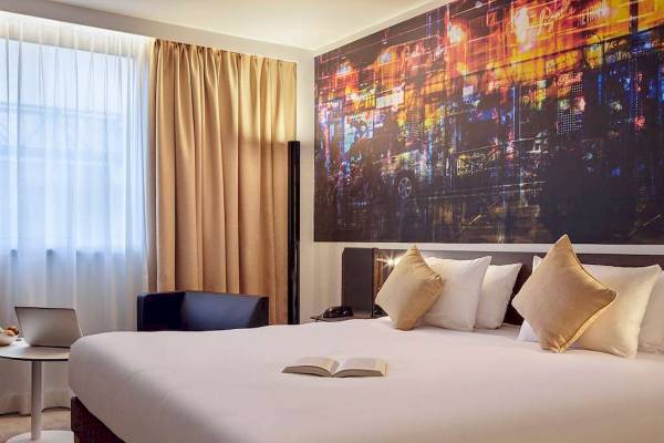 Hotelzimmer im Novotel Paris Centre Bercy mit großem Bett, offenem Buch und Laptop.
