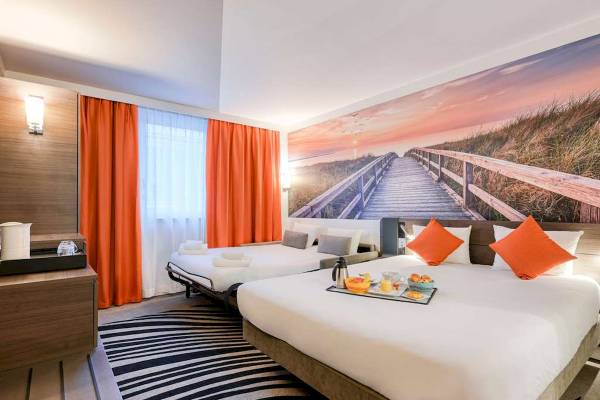 Innenansicht eines Hotelzimmers im Novotel Paris Centre Bercy mit zwei Betten, Frühstückstablett und Wandbild.