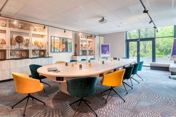 Konferenzraum im Novotel Paris Centre Bercy mit ovalem Tisch und bunten Stühlen.