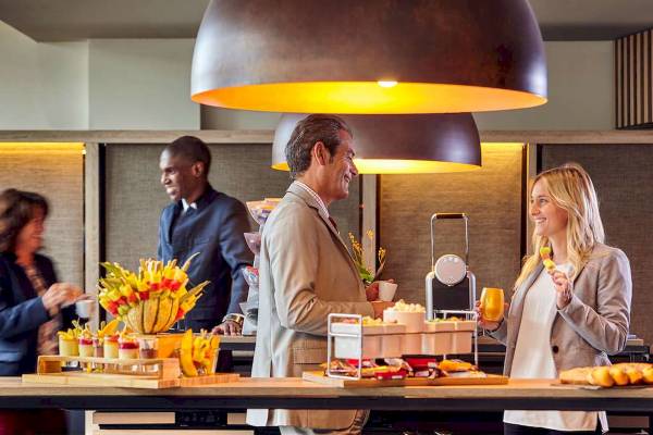 Ein Frühstücksbuffet im Novotel Paris Centre Bercy mit Gästen, die an einer Theke sitzen und essen.