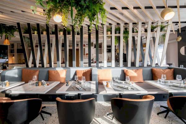 Innenansicht des Restaurants im Novotel Paris Centre Bercy mit Tischen, Stühlen und hängenden Pflanzen.