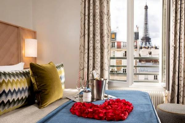 Hotelzimmer mit Eiffelturm-Aussicht und Valentinstagsarrangement mit Flasche, Gläsern und roten Rosenblättern.