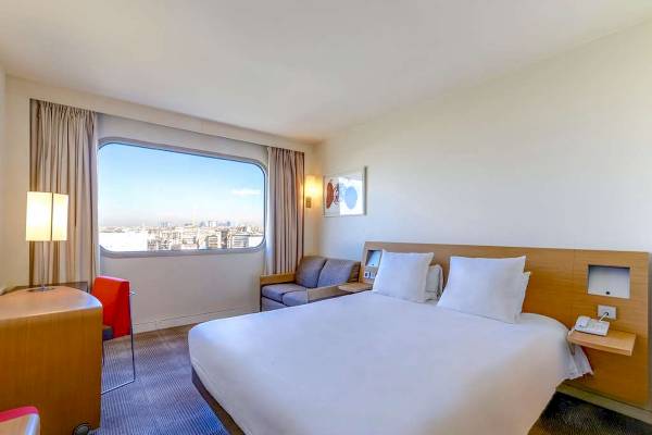 Innenansicht eines Zimmers im Novotel Paris Tour Eiffel mit einem großen Fenster, das die Stadt zeigt.