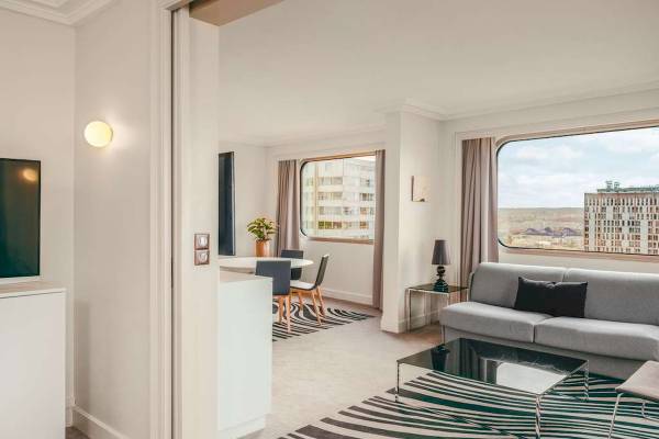 Innenansicht des Wohnbereichs im Novotel Paris Tour Eiffel mit Sofa, Tisch und Blick auf die Stadt