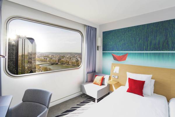 Hotelzimmer im Novotel Paris Tour Eiffel mit Blick auf die Stadt und großem Fenster.