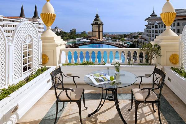 Balkon des Titanic Mardan Palace Hotels mit Tisch, Gartenblick und Pool im Hintergrund.