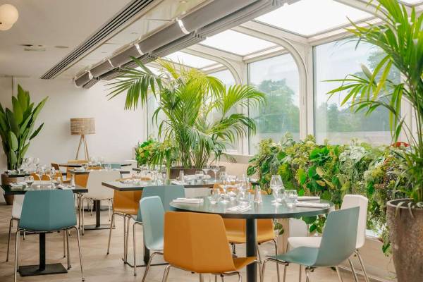Innenansicht des Restaurants im Novotel Paris Tour Eiffel mit runden Tischen, farbenfrohen Stühlen und großen Fenstern.