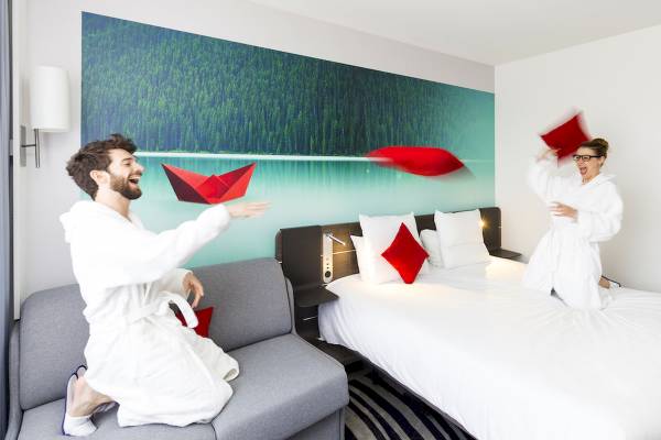 Paar im weißen Bademantel im Hotelzimmer Novotel Paris Tour Eiffel, sie spielen mit roten Papierbooten.
