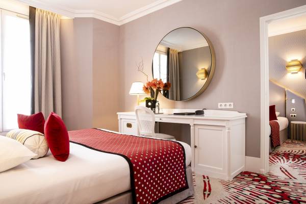 Ein stilvolles Zimmer im Hotel Victor Hugo Paris Kléber mit einem Bett, einem Schreibtisch und einem Spiegel.