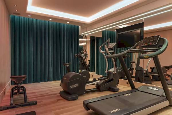 Fitnessraum im Victor Hugo Paris Kléber Hotel mit Laufband, Rudergerät und blauen Vorhängen.