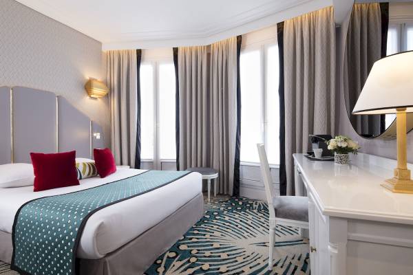 Ein elegantes Hotelzimmer im Victor Hugo Paris Kléber mit Bett, Schreibtisch und Fenstern.