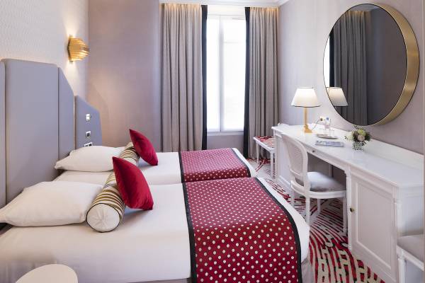 Zwei Doppelbetten mit roten und weißen Punkten in einem eleganten Hotelzimmer, Victor Hugo Paris Kléber.