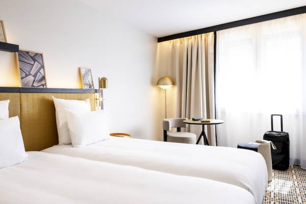 Doppelzimmer im Mercure Paris Bercy Bibliothèque mit zwei Betten, Nachttischen und einem Reisekoffer.