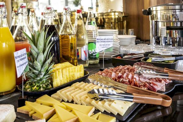 Frühstücksbuffet im Mercure Paris Bercy Bibliothèque mit verschiedenen Käsesorten, Schinken, Tomaten, Orangensaft und weiteren Getränken.