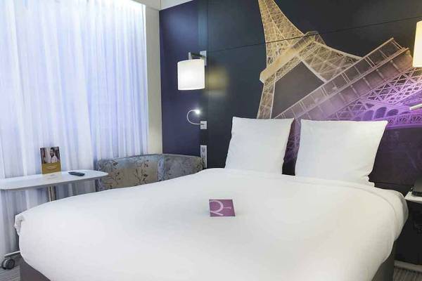 Doppelbett im Hotelzimmer mit Eiffelturm-Hintergrund im Mercure Paris Centre Tour Eiffel