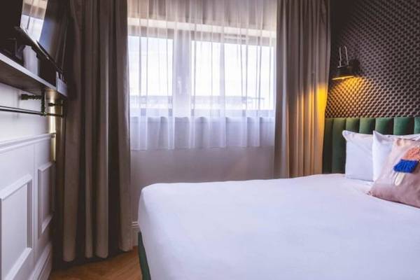 Ein modernes Hotelzimmer mit weißem Bett, Kissen und Fernseher an der Wand.
