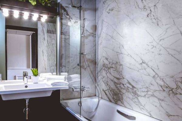 Badezimmer im ReMIX Hotel mit weißen Marmorwänden, Badewanne, Waschbecken und Spiegel.