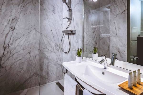 Badezimmer im ReMIX Hotel mit Marmorwänden, Duschbereich und Waschbecken.