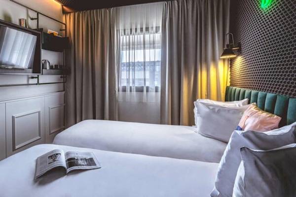 Ein modernes Hotelzimmer im ReMIX Hotel mit zwei Betten, einer offenen Zeitschrift und einer Wand mit Fernseher und Lampe.
