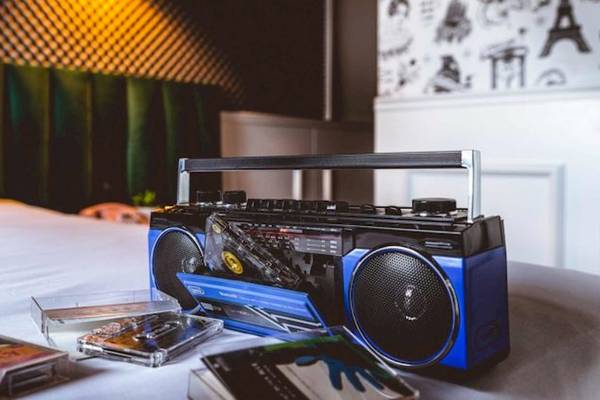 Ein Boombox auf einem Bett im ReMIX Hotel neben Musikkassetten und einem Kissen.