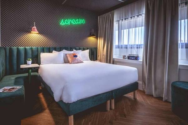 Schlafzimmer im The ReMIX Hotel mit grünem Kopfteil, weißem Bett, Nachttisch und Neon-Schriftzug Scream.