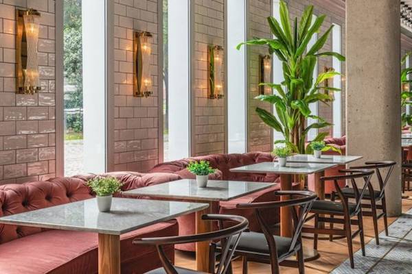 Innenansicht des ReMIX Hotel Restaurants mit roten Sofas, Holztischen, grünen Pflanzen und weißen Ziegelwänden.