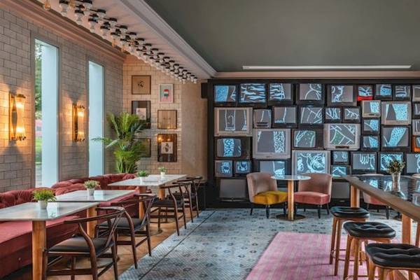 Innenraum des ReMIX Hotels mit vielen Fernsehern an der Wand, Tischen und Stühlen, Pflanzen und Lampen.