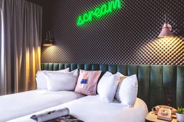 Schlafzimmer mit zwei Betten, grüner Wand und Neon-Schild, das 'dream' sagt.