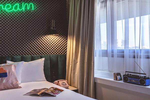 Zimmer im ReMIX Hotel mit grünem Bett, Neon-Schild 'dream', Kissen, Radio und Fenster mit Vorhängen.