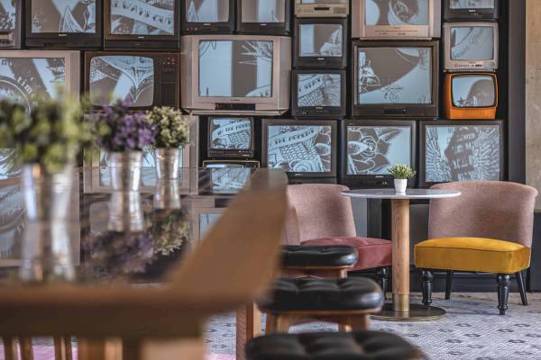 Barbereich des ReMIX Hotels mit Fernsehern an der Wand und farbenfrohen Stühlen.