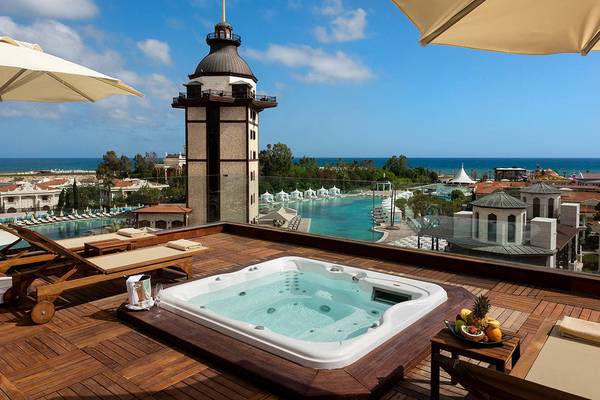 Hotelterrasse mit Jacuzzi und Ausblick auf das Meer und eine historische Turmstruktur.