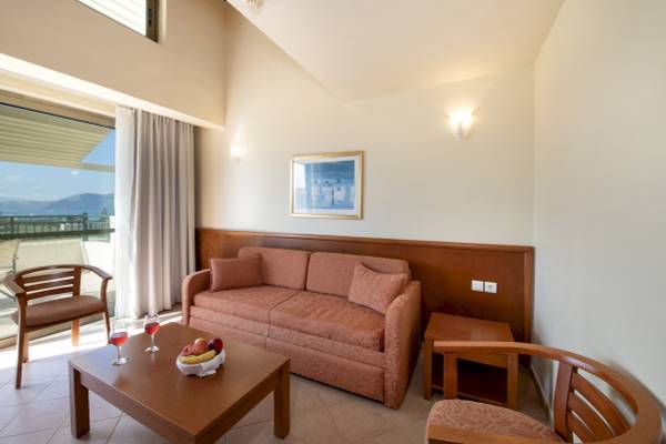 Wohnzimmer im Hydramis Palace Beach Resort mit einem Sofa, zwei Sesseln, einem Tisch und einem Balkon mit Meerblick.