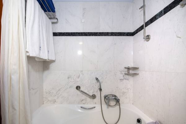 Badezimmer mit Dusche und Badewanne im Hydramis Palace Beach Resort mit weißen Marmorfliesen und blauen Akzenten.