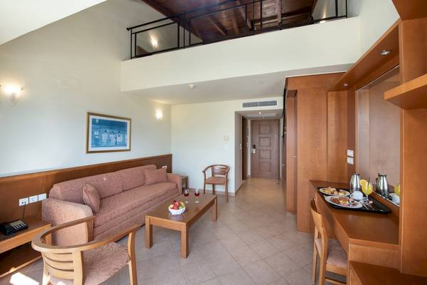 Innenansicht eines Hotelzimmers mit Sofa, Tisch, Frühstückstablett und offenem Balkon.