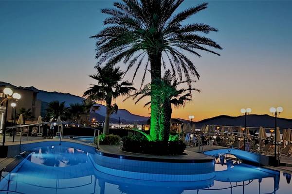 Der Poolbereich des Hydramis Palace Beach Resorts bei Sonnenuntergang mit beleuchteten Palmen und einem blau beleuchteten Wasserbecken.