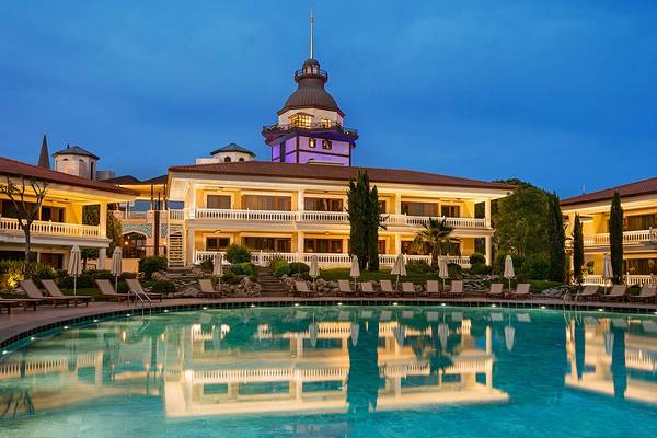 Nachtansicht des Titanic Mardan Palace Hotels mit einem großen Pool und umliegenden Loungeliegen.
