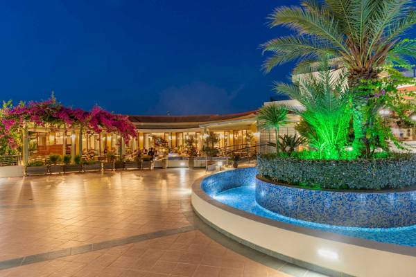Abendlicher Eingang zum Hydramis Palace Beach Resort mit leuchtenden Pflanzen und Palmen.