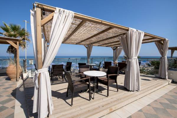Terrasse mit Tischen und Stuelzen am Strand mit Blick auf das Meer.