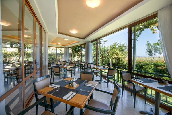 Innenansicht des Restaurants im Hydramis Palace Beach Resort mit gedeckten Tischen und Blick auf den Garten.