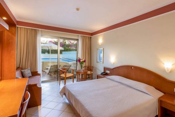 Hotelzimmer mit einem großen Bett und einer Terrasse, die auf einen Poolbereich führt.