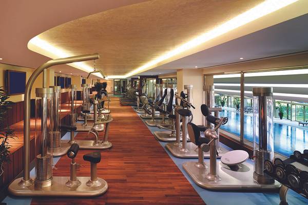 Innenansicht des Fitnesscenters im Titanic Mardan Palace mit Cardiogeräten und Blick auf den Pool.