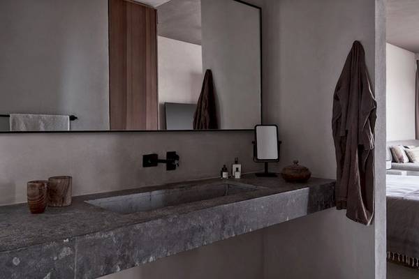 Innenansicht des Badezimmers im Casa Cook El Gouna Hotel mit Betonwaschbecken, Spiegel und einem Bett im Hintergrund.
