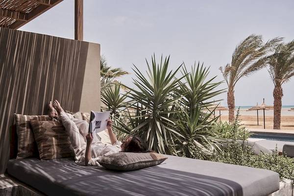 Frau liest ein Buch auf einem Bett im Freien neben einem Pool und Palmen