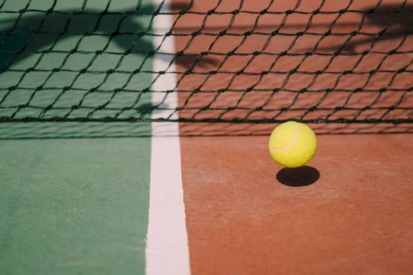 Ein gelber Tennisball auf einem Tennisplatz mit grünem und rotem Boden.