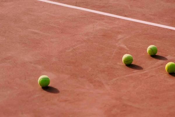 Vier Tennisbälle auf einem roten Tennisplatz neben einer weißen Linie.