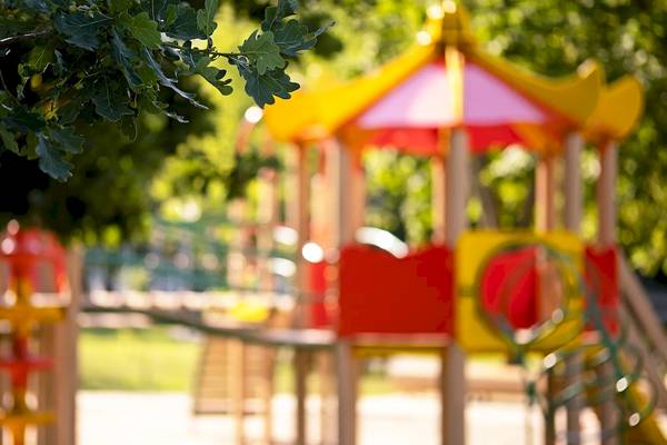 Foto eines bunten Kinderspielplatzes im Freien mit Bäumen im Hintergrund.