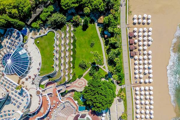 Luftaufnahme des Sonnenaufgang Queen Luxus Hotels mit Strand, weißen Sonnenschirmen und grüner Landschaft