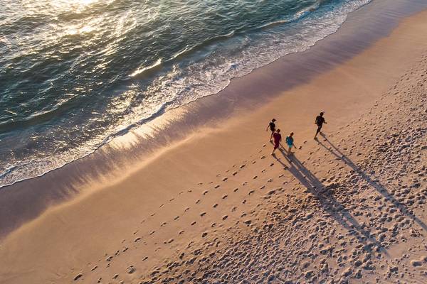 Familie läuft am Strand entlang bei Sonnenaufgang, Wasser im Hintergrund