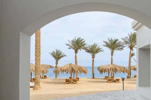 Ausblick auf den Strand des Serry Beach Resorts mit weißen Gebäuden, Sonnenliegen, Palmen und Meer